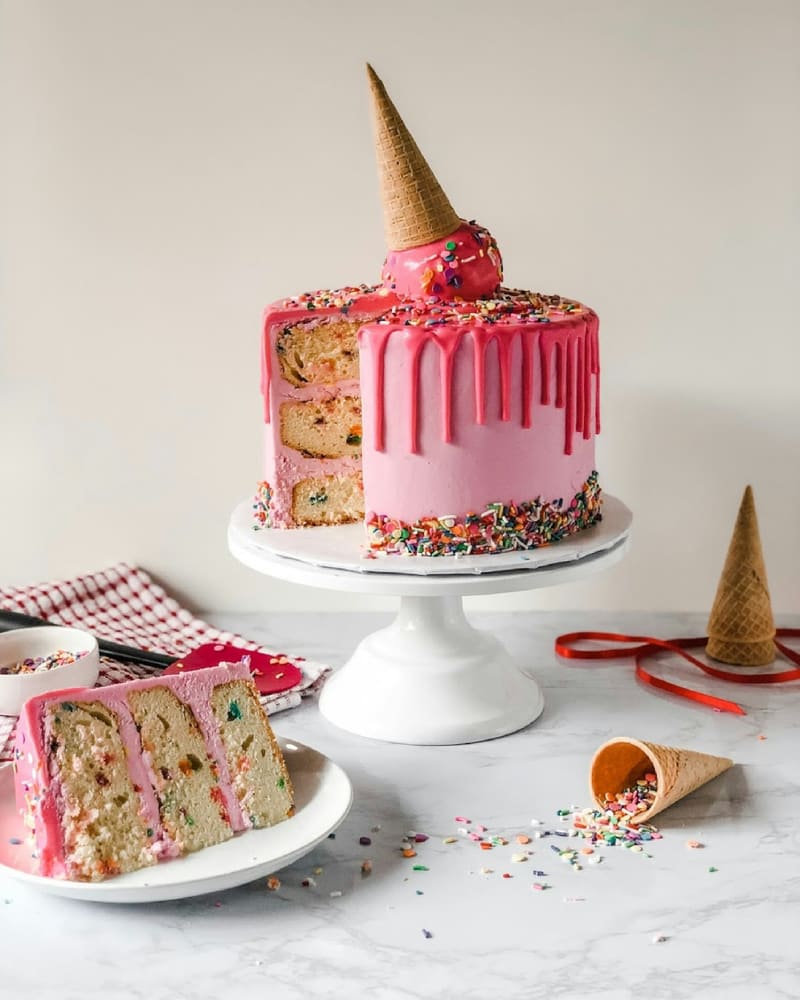 Een roze ijstaart met een omgekeerd hoorntje erop en spikkels eromheen